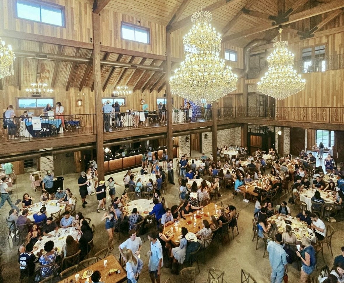 A large crowd of people sitting at tables in a spacious rustic banquet hall.