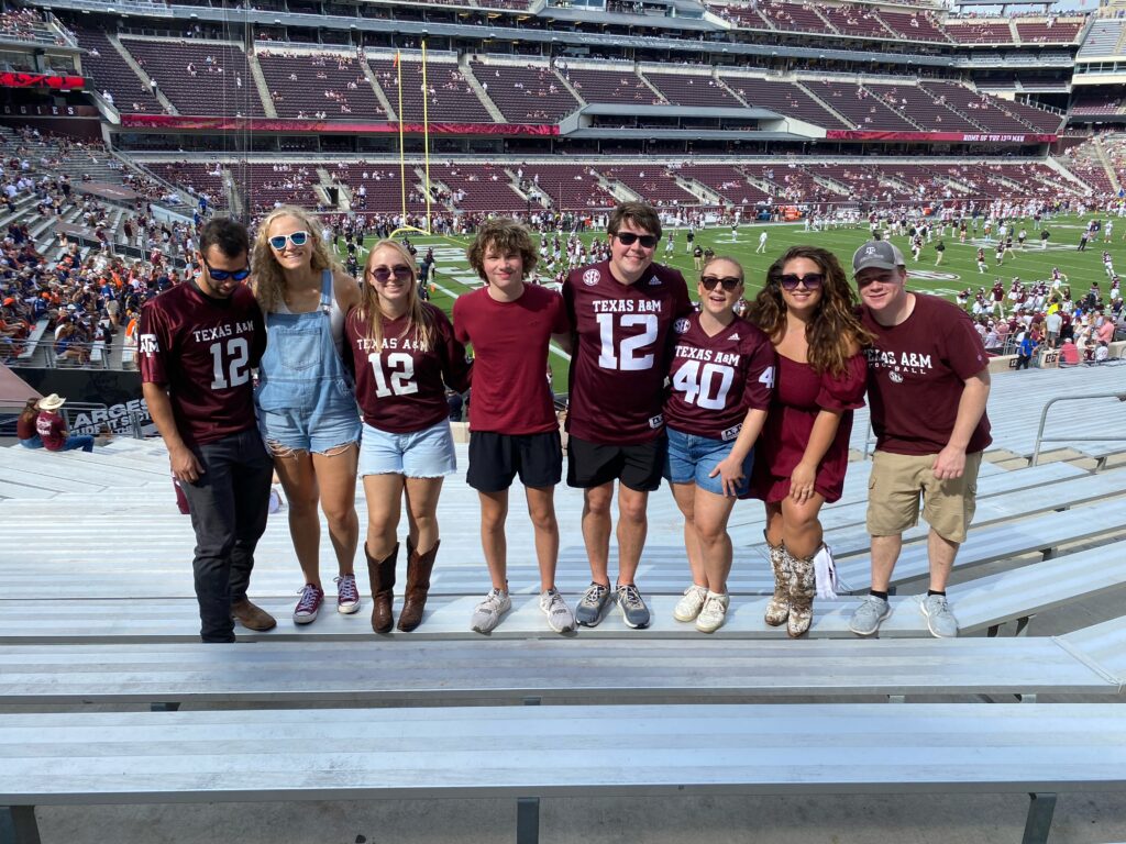 A group of eight Texas A&M students in game day attire standing in the Kyle Field stadium bleachers.