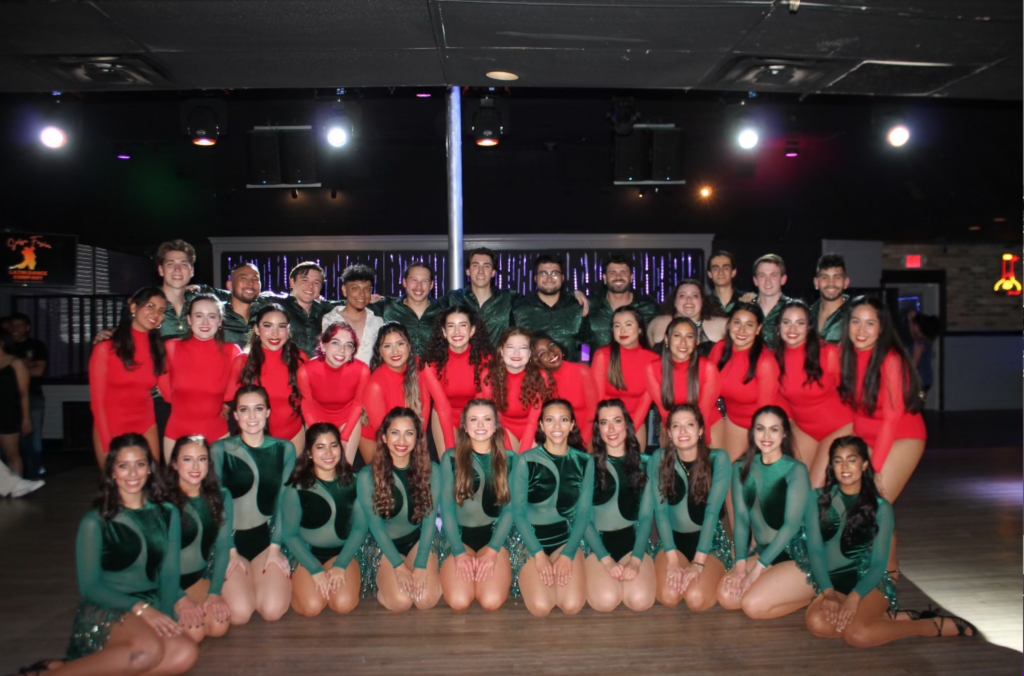 About 30 college students posing for a group photo at a dance competition in green (back and front row) and red (middle row) costumes.