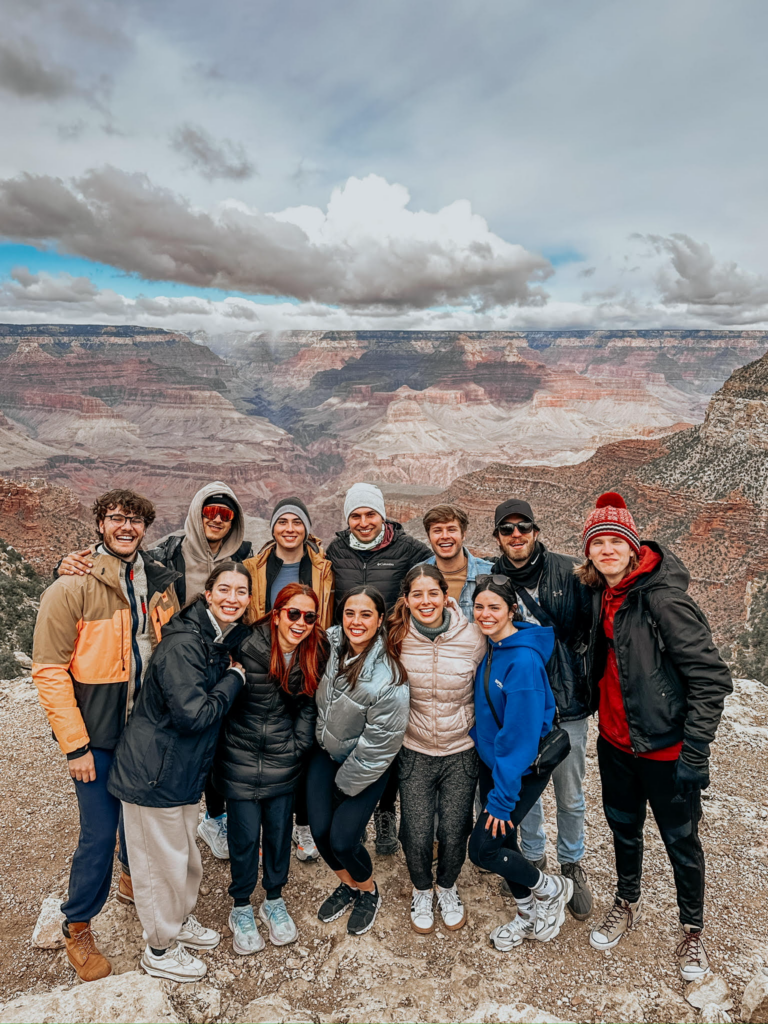 A group of twelve college students in winter clothes posing in front of the Grand Canyon.