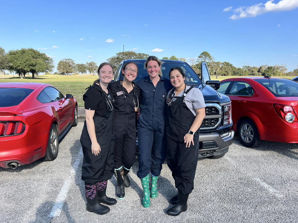 Priya and three of her friends stand together smiling in a parking lot with vehicles in the background