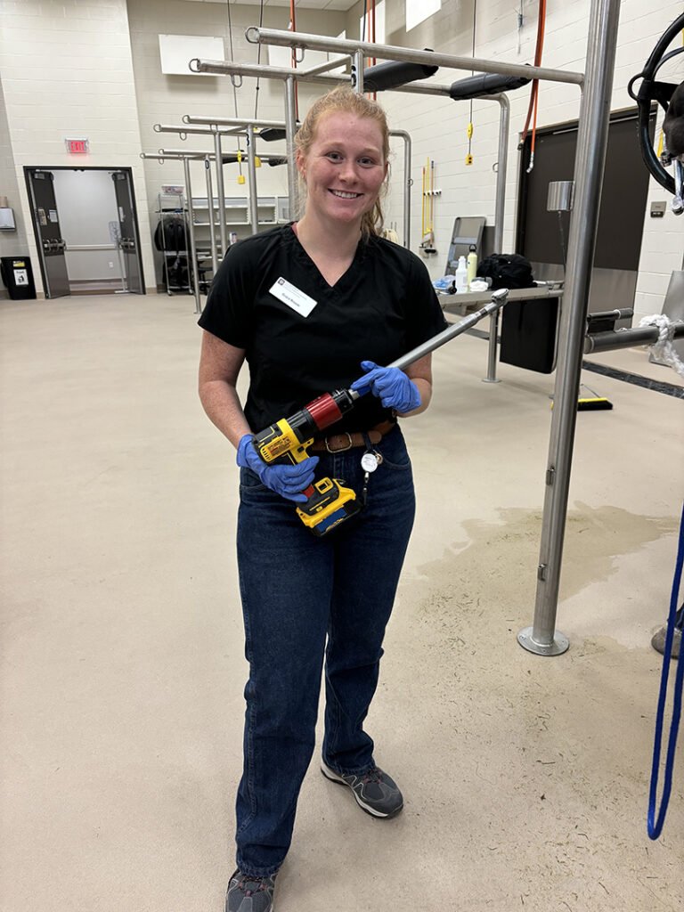 Grace holds a dental drill inside an equine barn