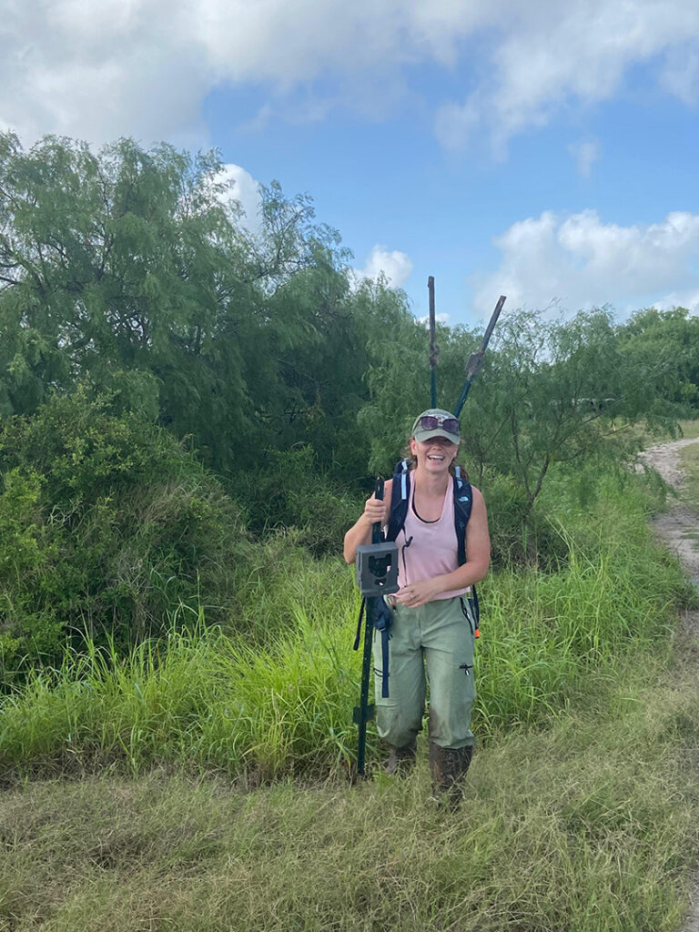 Anna stands in a grassy field holding research equipment as she conducts field work