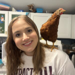 Katie smiles at the camera with a brown chicken perched on her shoulder inside a clinic