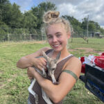Grace smiles as she holds a small kangaroo in a grass enclosure.