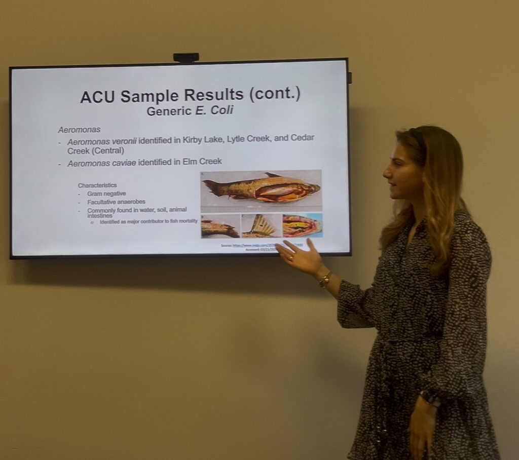 Emma presents her research in a classroom with a screen next to her that displays her research findings.