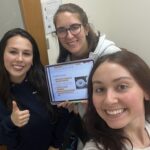 Annabelle takes a selfie with two friends. One is holding an iPad displaying a scientific presentation.