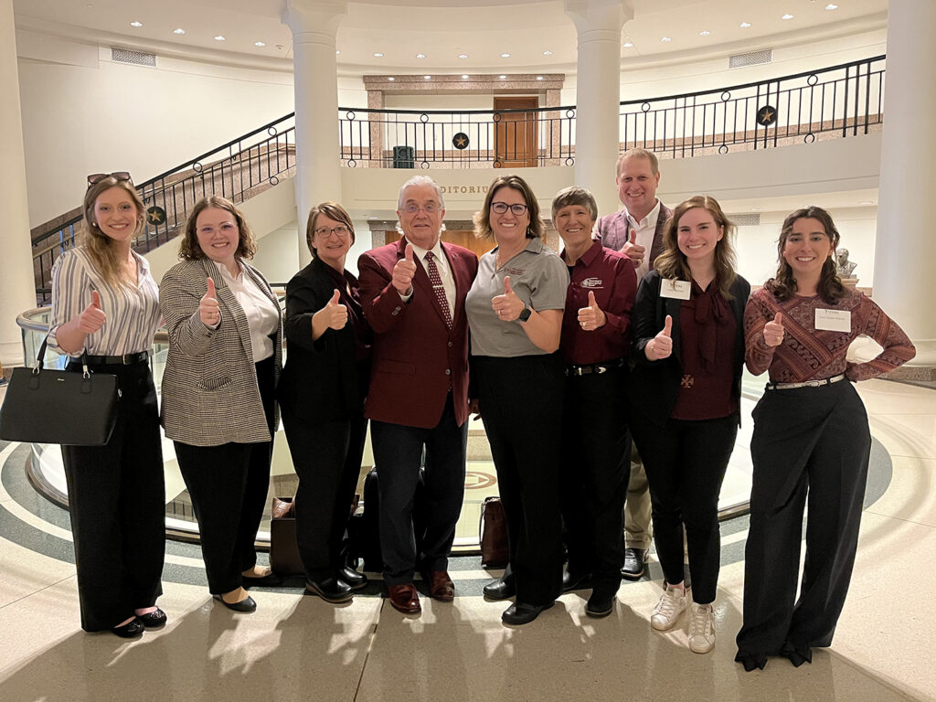 VMBS faculty, staff, and students stand inside the Texas State Capitol giving a thumbs up.