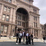 Hope stands with four other individuals posing in front of the Texas State Capitol building.