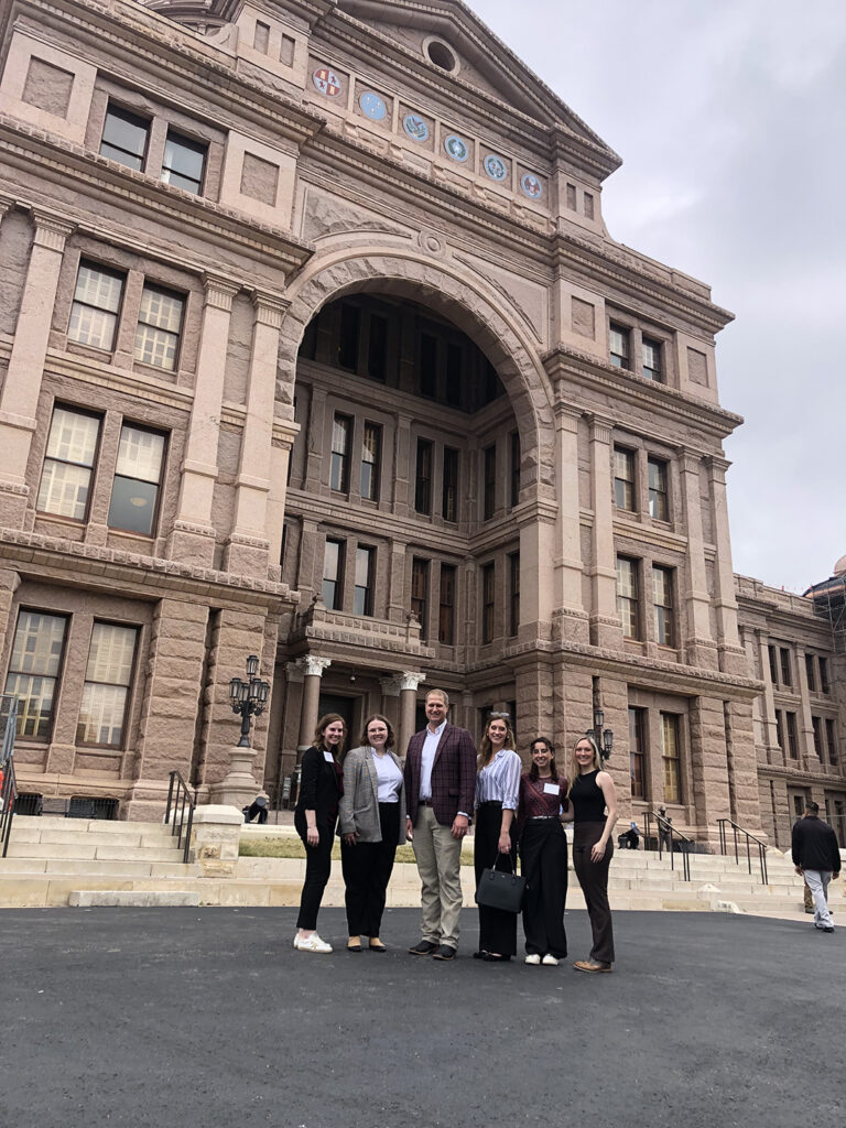 Hope stands with four other individuals posing in front of the Texas State Capitol building.