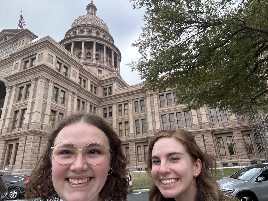 Hope and her peer take a selfie as they smile in front of the Texas State Capitol building.