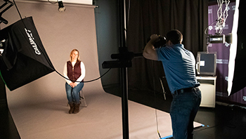 woman sits for a portrait with photographer behind camera in studio