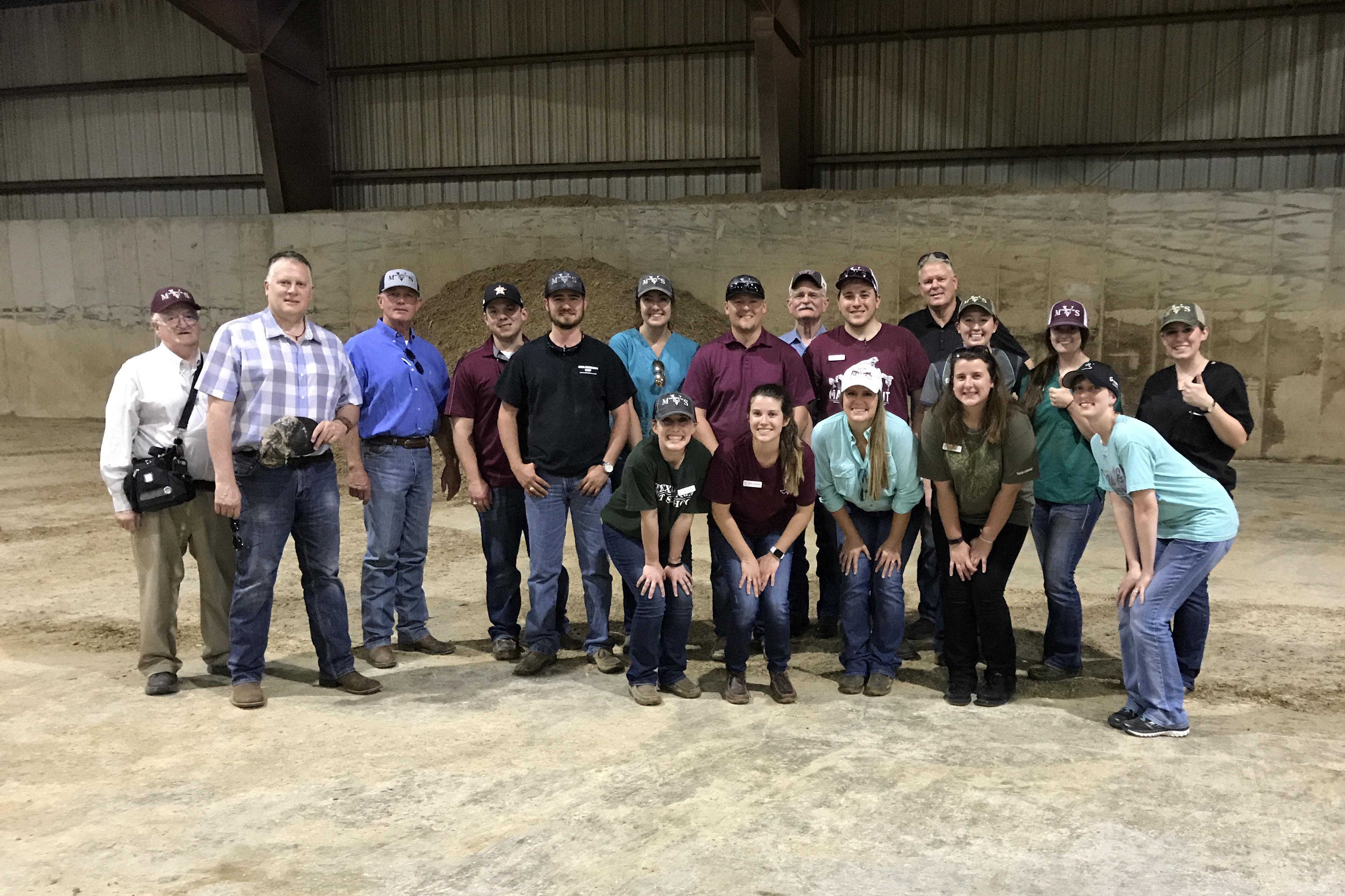 A group of students and VERO leaders stand in an empty barn, smiling for the camera