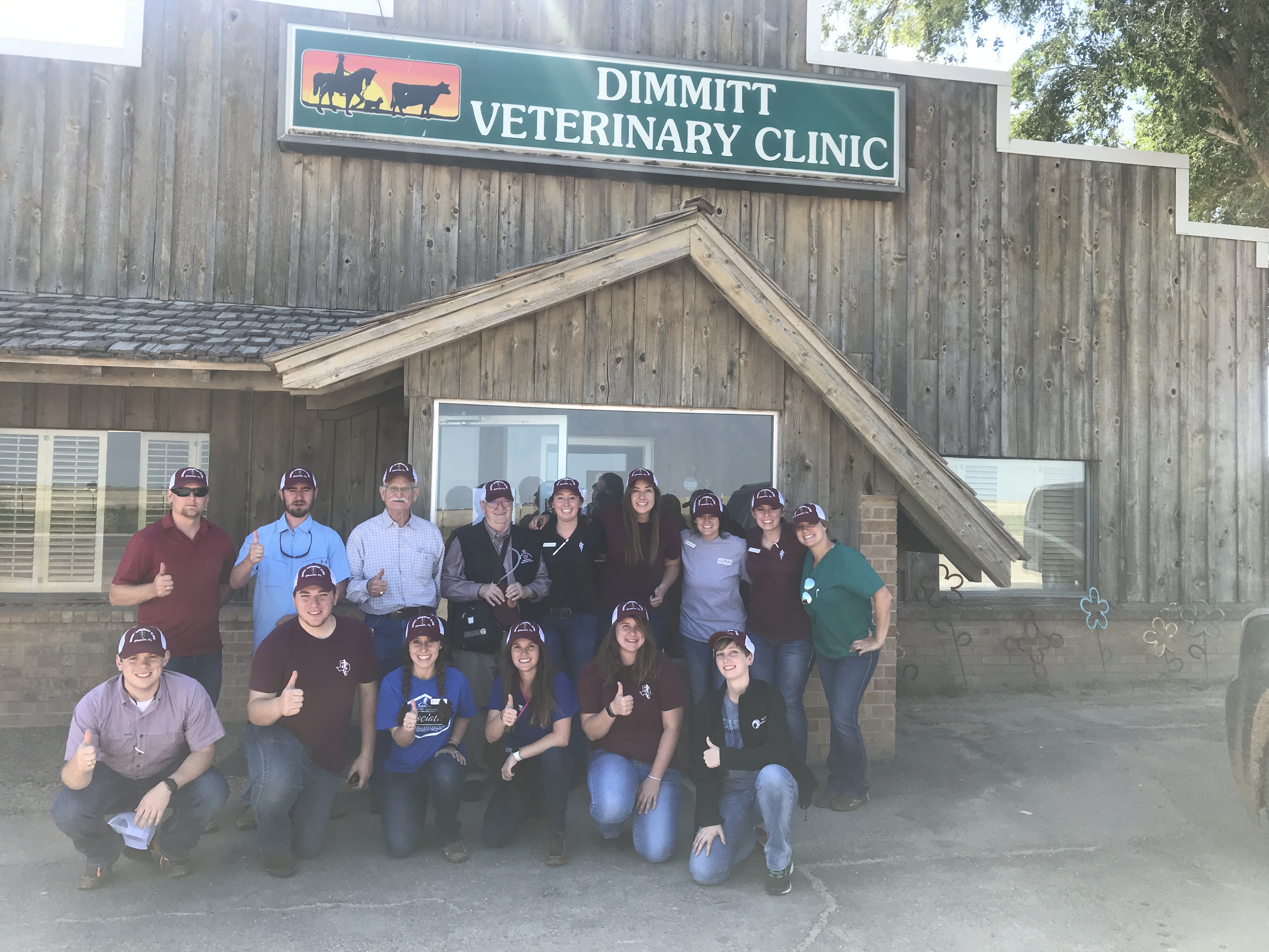 A group of students and VERO tour leaders give thumbs up outside the rustic Dimmit Veterinary Clinic