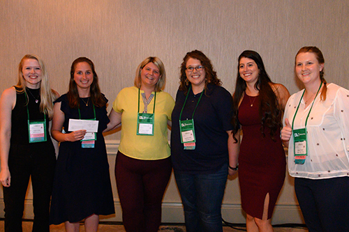 Six female students stand in a row, one holding a check