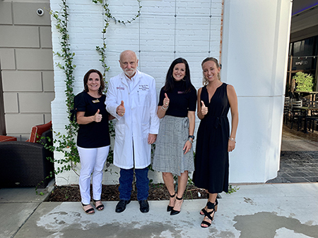 Chastity Carrigan, Dr. Glen Laine, Trudy Bennett, and Jordan Kuhn give thumbs up in front of a white brick wall