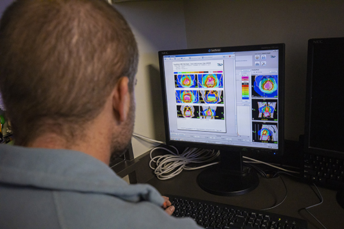 Radiation oncologist Dr. Michael Deveau watches a screen of colorful scans to monitor Lady as she undergoes her TomoTherapy treatment