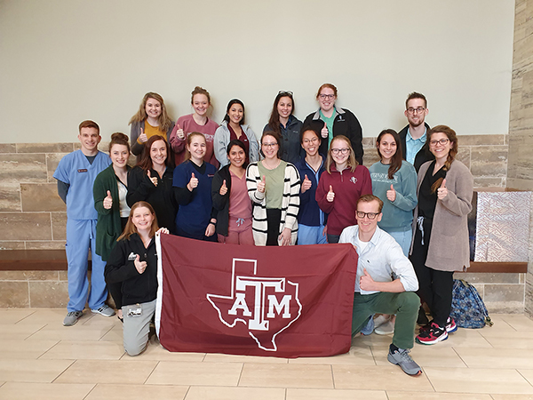 A group of students and faculty hold a Texas A&M flag