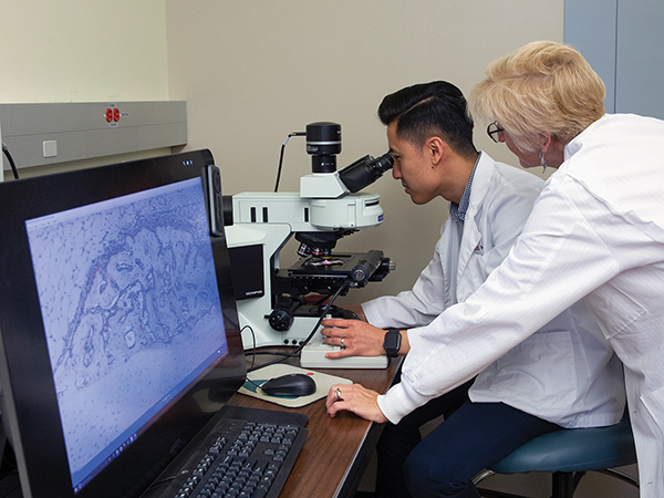 Duc Nguyen looks into a microscope while Dr. Dana Gaddy watches