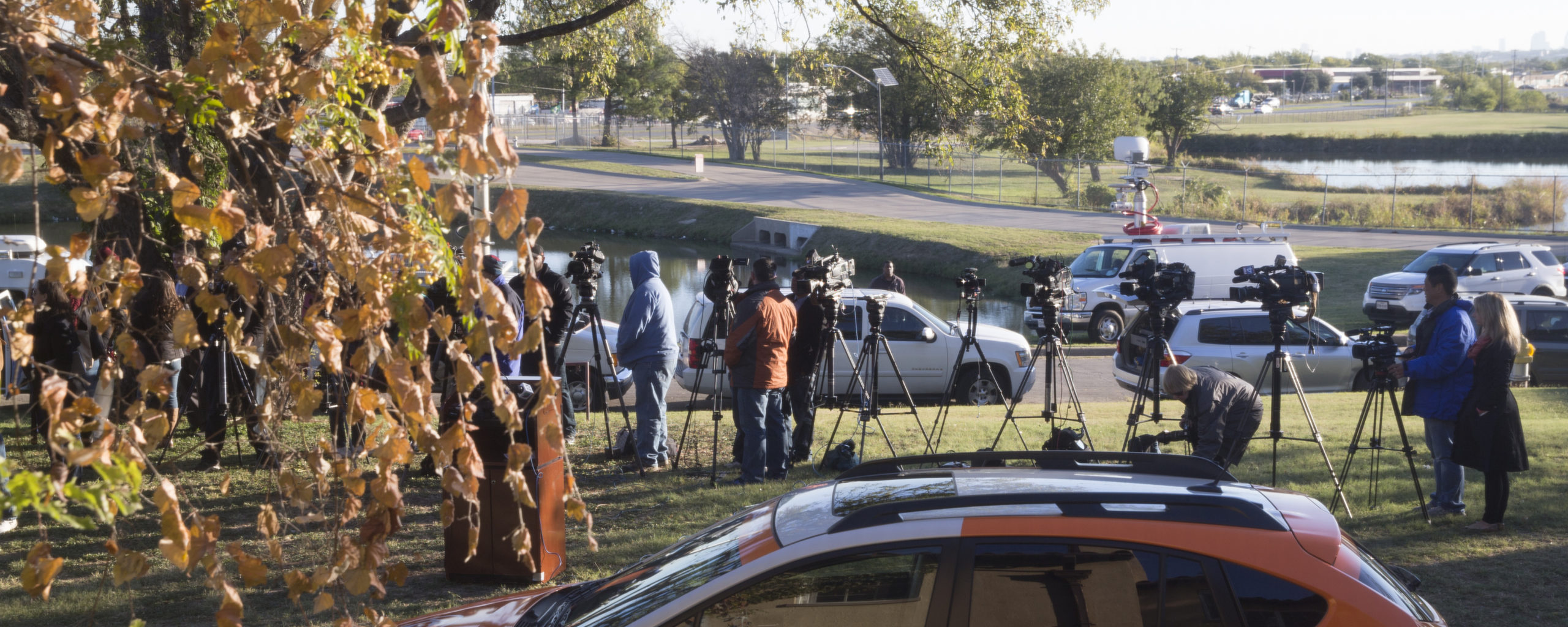 News reporters and camera operators with news vehicles gather outside for a press conference