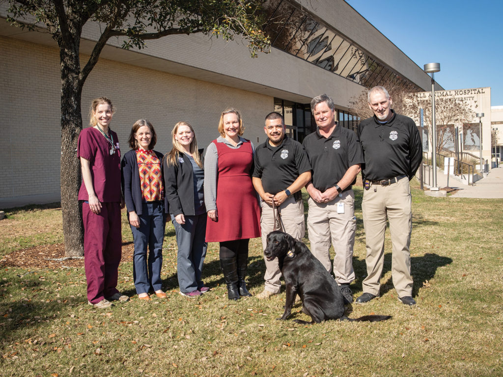 7 people and a black K-9, who received funds from LeBlanc's gift, in front of the small animal hospital