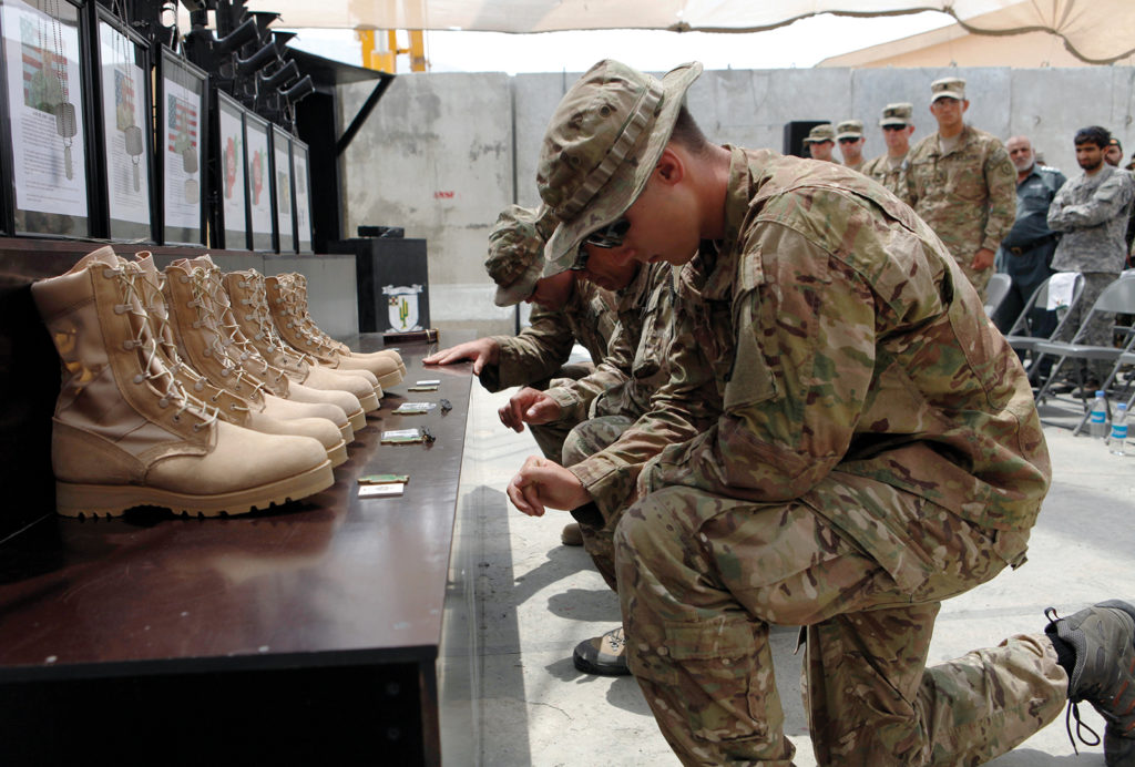 Soldiers kneeling in front of a row of Army boots