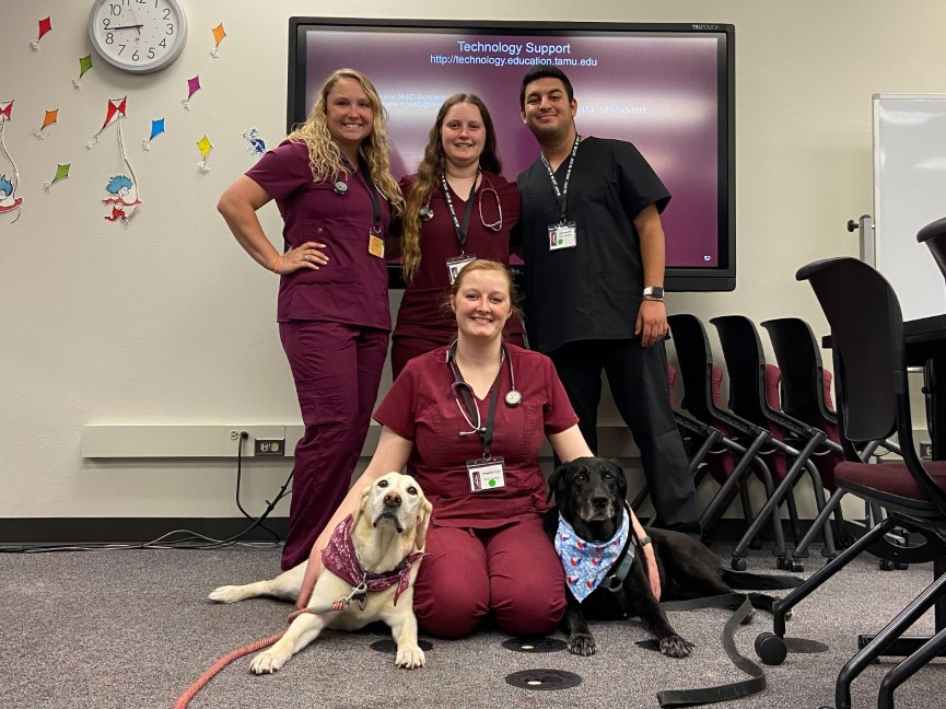 four students in scrubs with two dogs