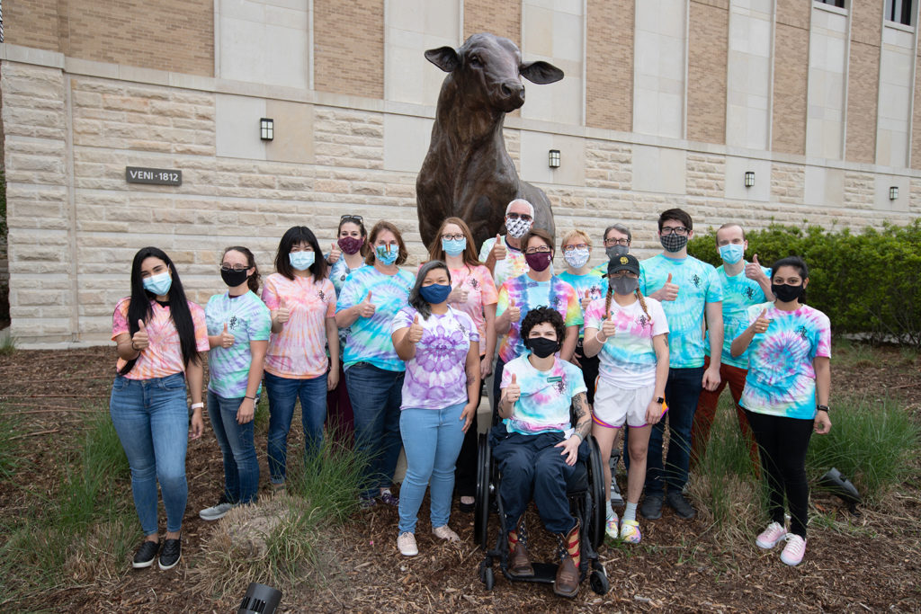 group of people in tye dye shirts in front of bull statue