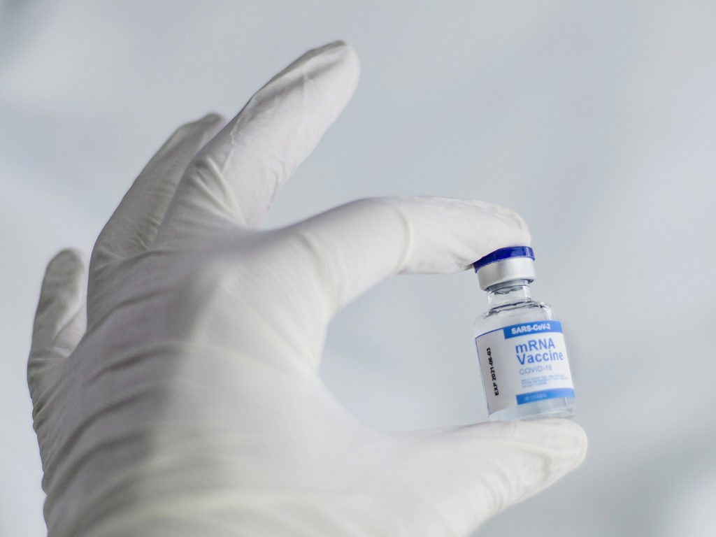A hand in a white glove holding up a bottle of mRNA vaccine for SARS-CoV-2