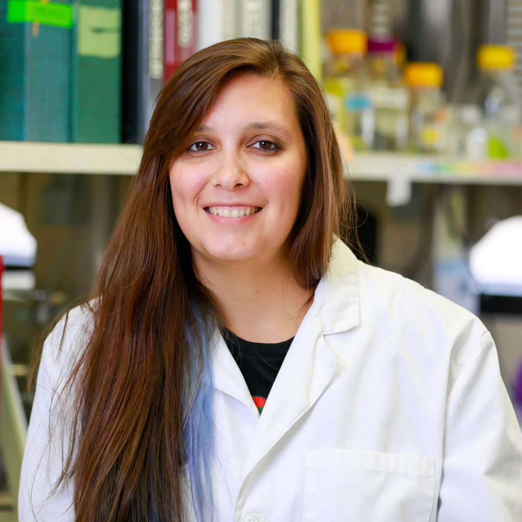 Caitlin Castaneda in a white coat sitting in a lab