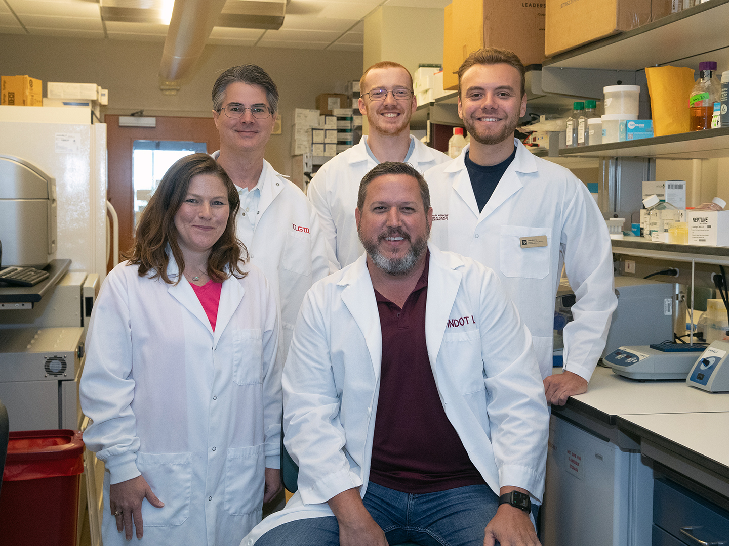 Five scientists wearing white coatsin the Dindot lab