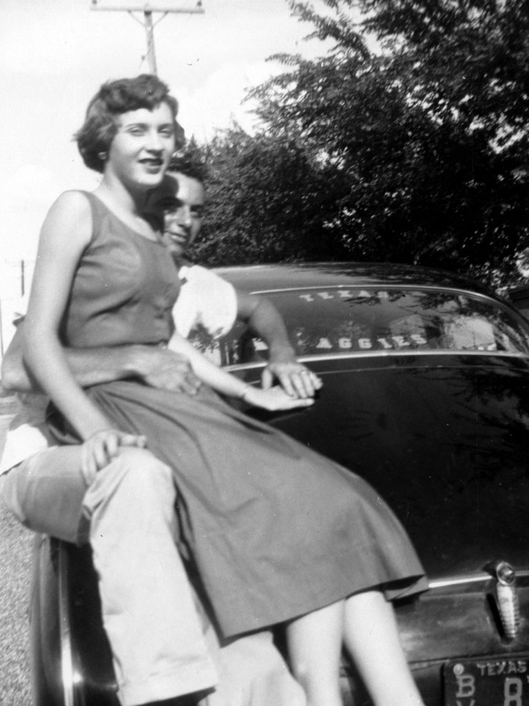 Young Joyce sitting on young Bill's lap on the hood of a car, black and white 