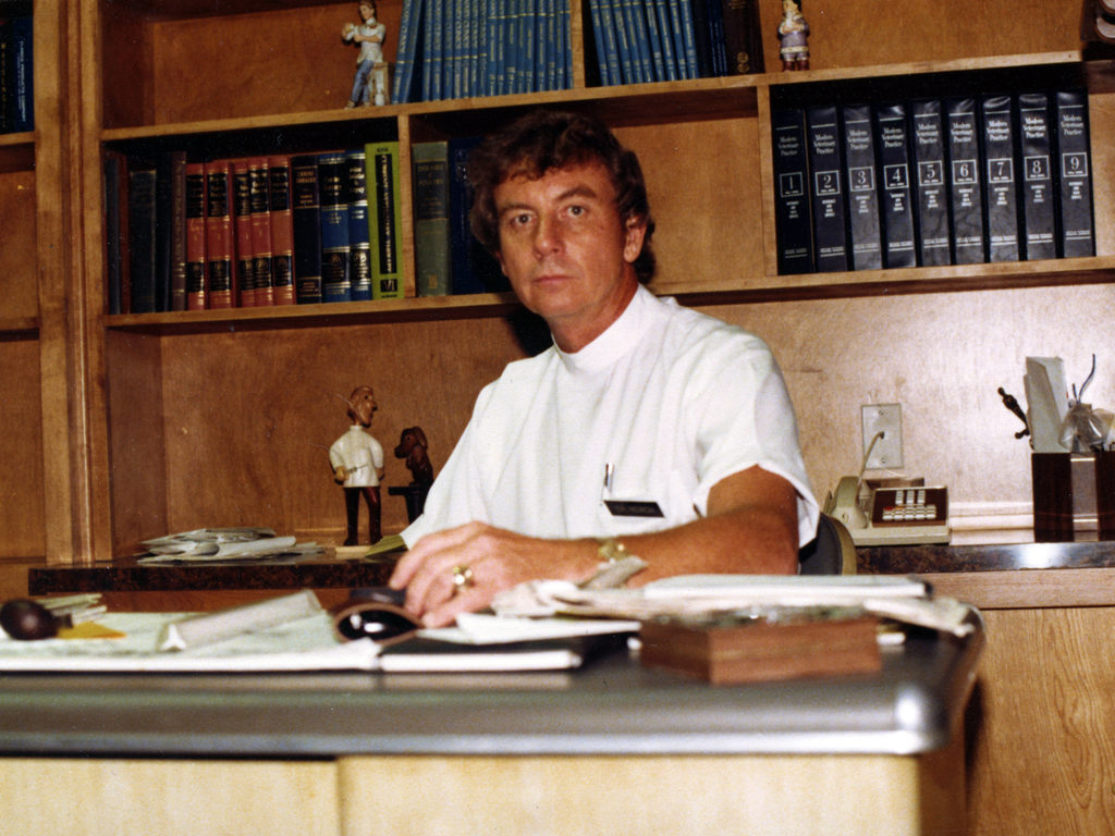 Young Bill Roach sitting at a desk in a veterinary office