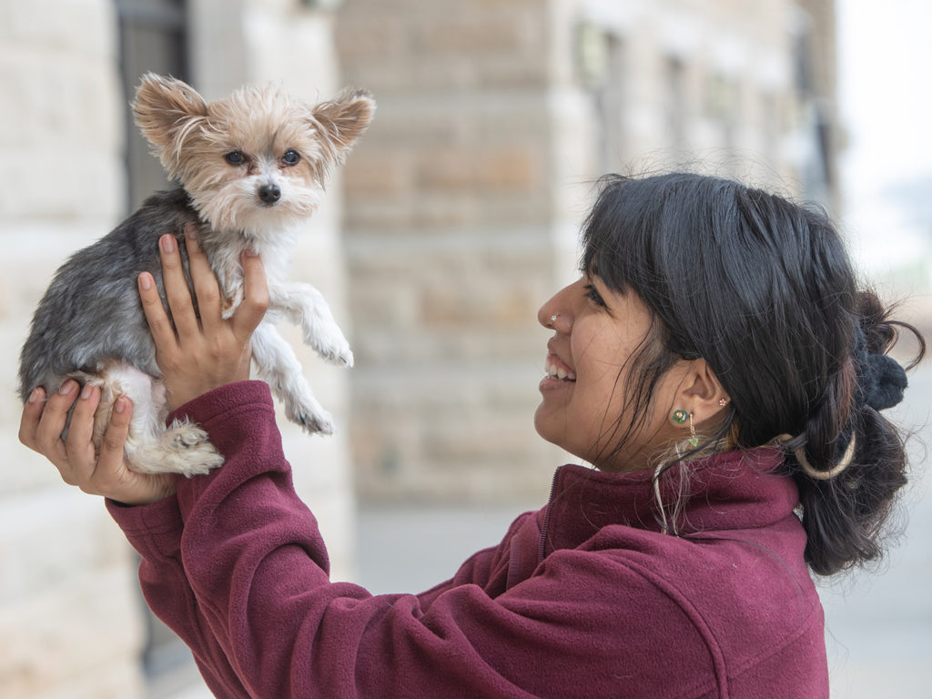 Veterinary student wearing maroon holding a small yorkie up in the air and smiling at him