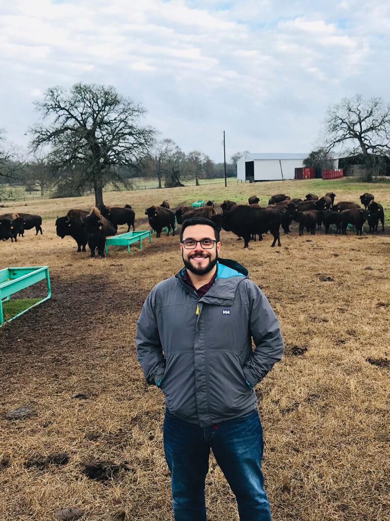Verocai in a field with a herd of bison behind him