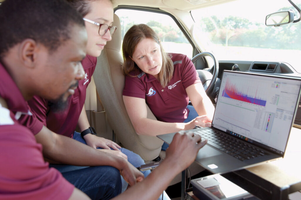 Three people in maroon Texas A&M Superfund Center shirts reviewing air quality data on a computer in the mRAPiD van