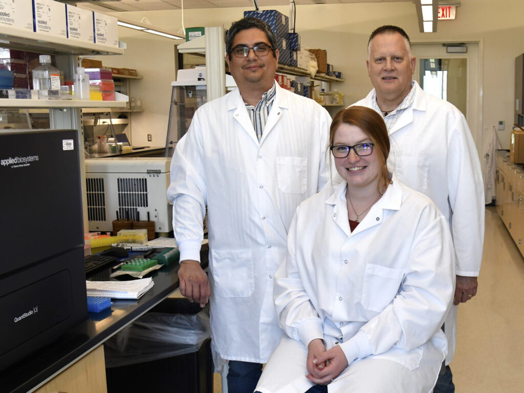Dr. Robert Valeris-Chacin, Dr. Paul Morley, and student Ali Olsen-Gerlach wearing white coats in a research lab