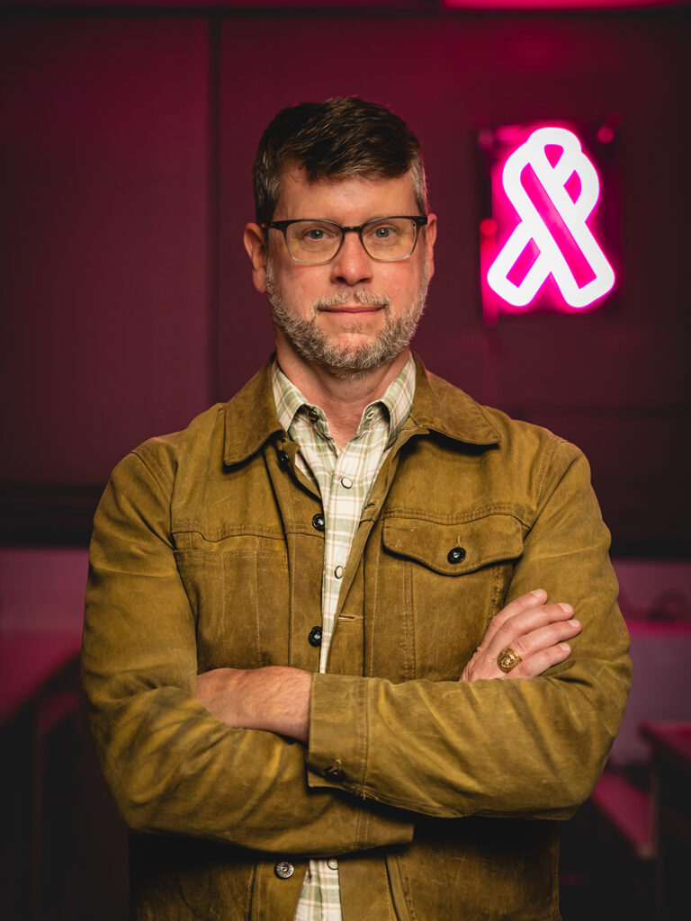 Dr. Weston Porter in front of a neon pink breast cancer ribbon sign