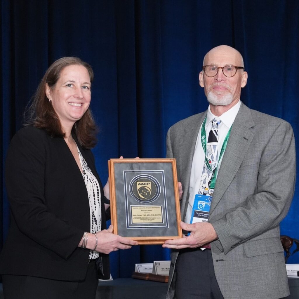 A woman handing a framed plaque to a man in a gray suit.