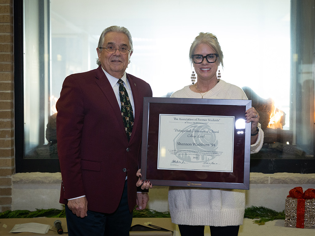 A man in a maroon suit jacket standing beside a woman holding a framed award certificate. 