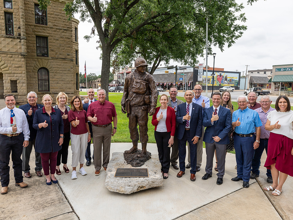 A group of leaders from Texas A&M and McCulloch County stand in front of a courthouse making the gig 'em gesture.