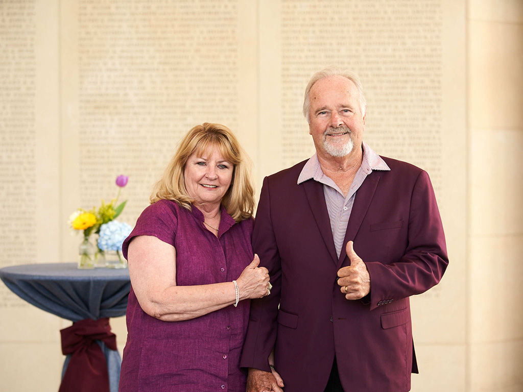 A man and woman in maroon clothes giving the gig 'em gesture.