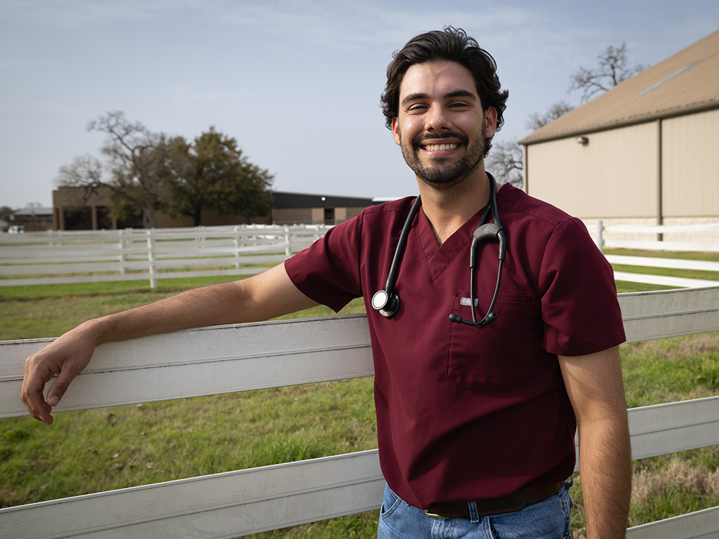 A student in a maroon shirt leaning on a fence.