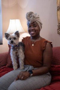 A young woman in an orange shirt with a small dog in her lap.