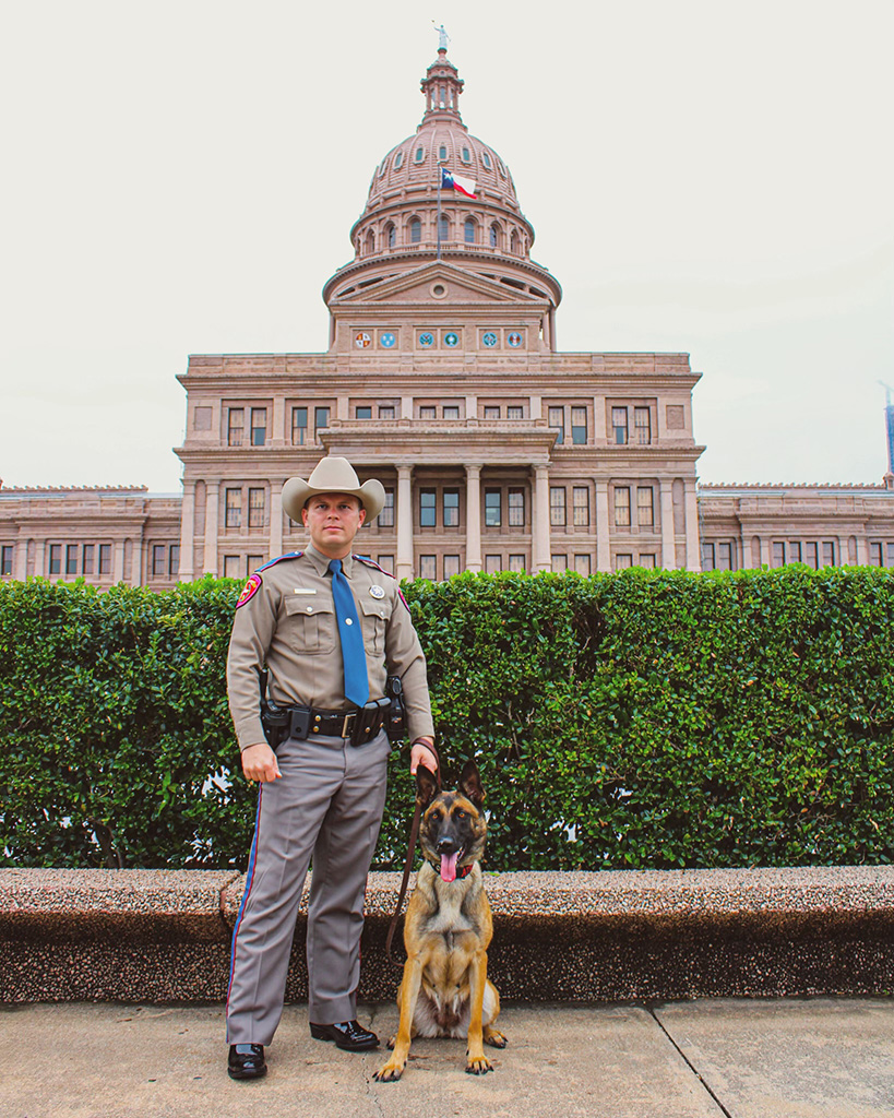 An officer and a K9 standing in front of the Texas state capitol building.