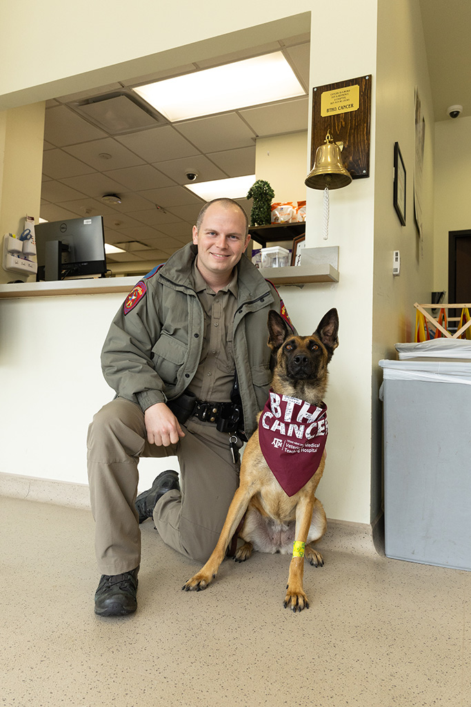 A K9 and her handler kneeling beneath the cancer bell at a veterinary hospital.