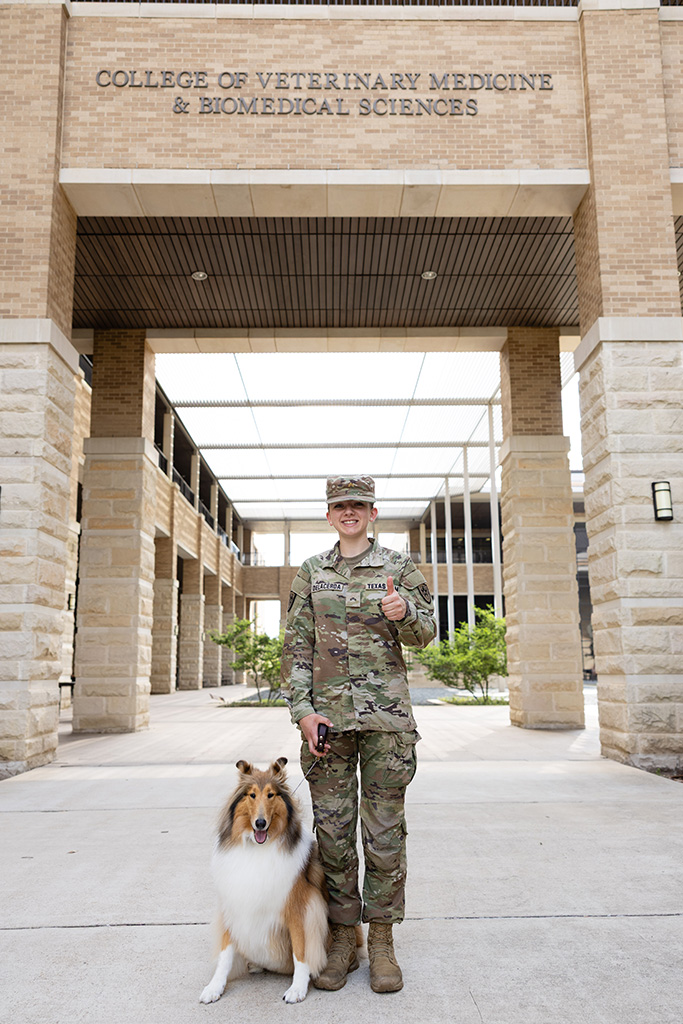 A young woman in military fatigues standing beside a rough collie.