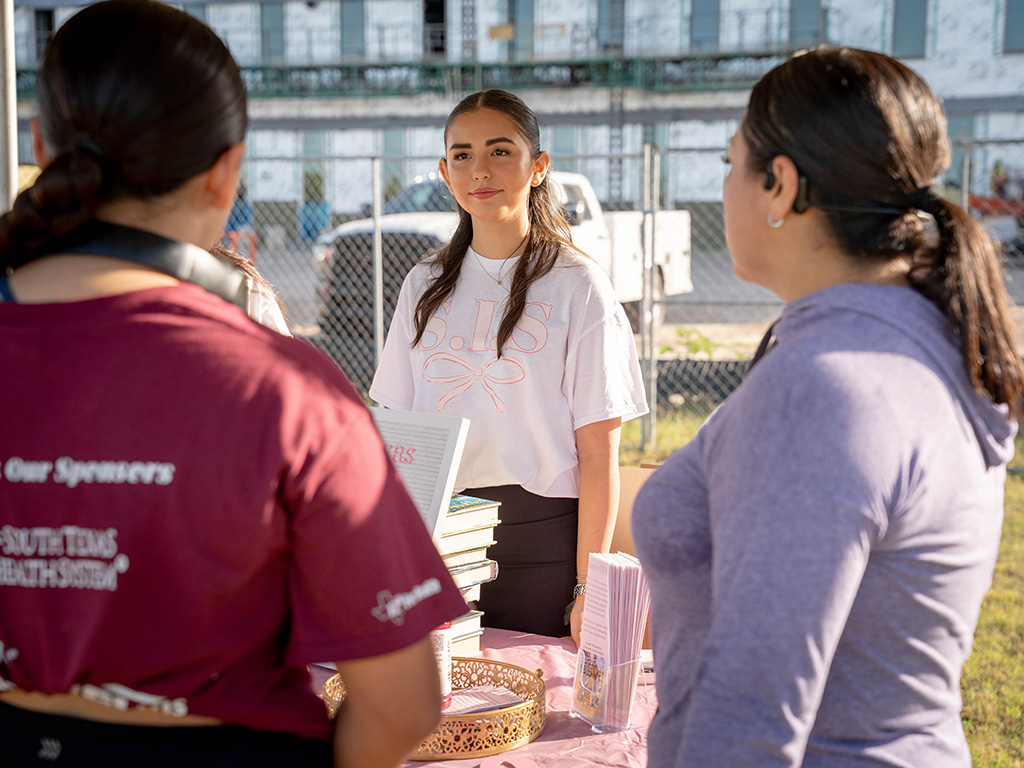 A girl standing behind a table at a student fair.