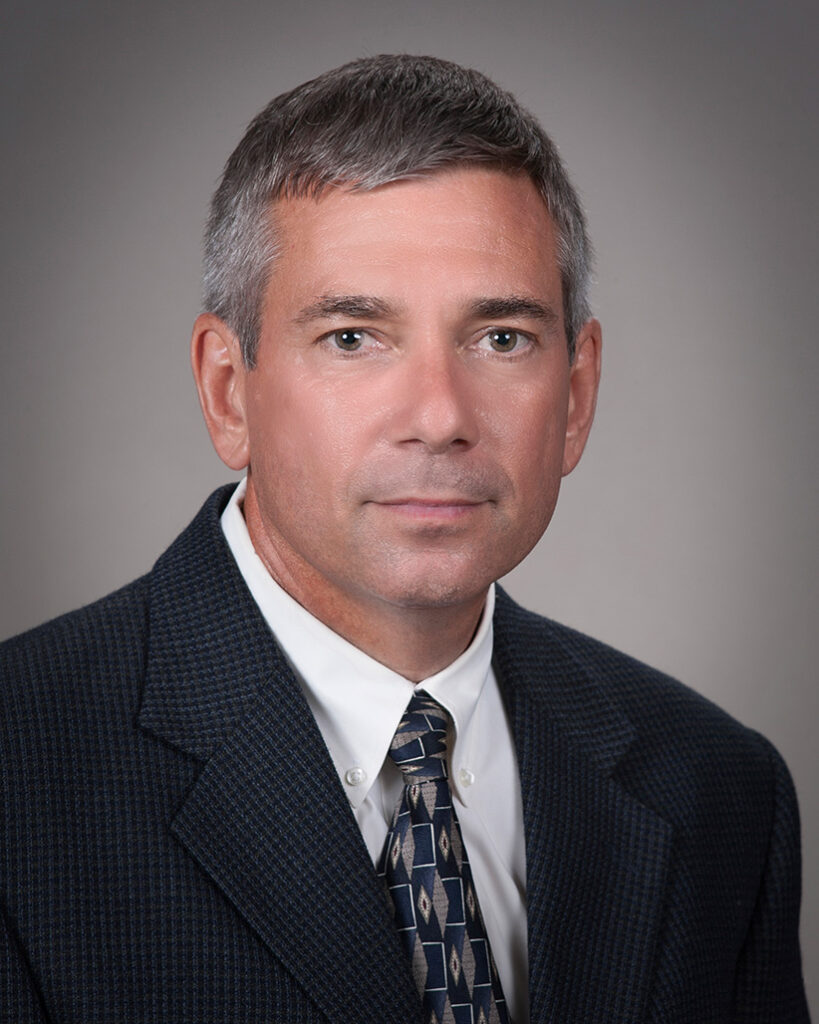 A university headshot of a male professor in a black suit.