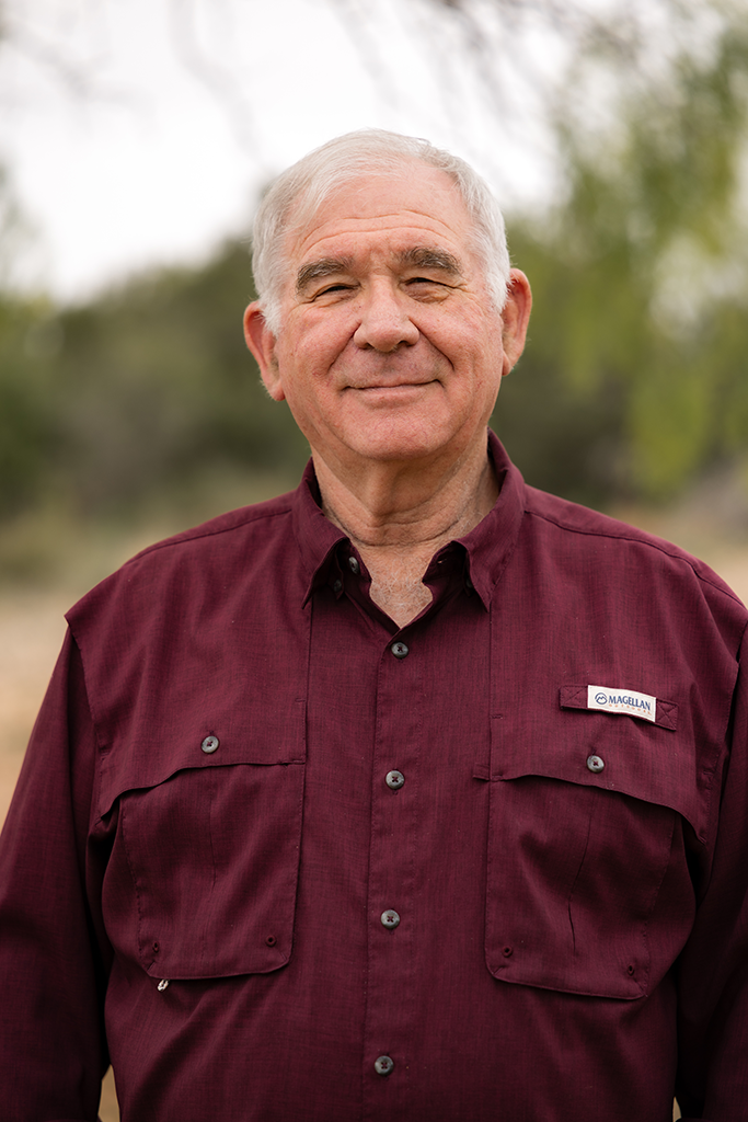 A headshot of a man standing outdoors wearing a maroon button-down.